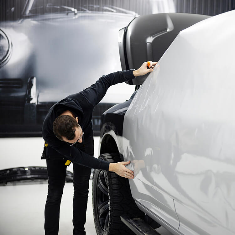 Installer positioning light gray vinyl along a vehicle side