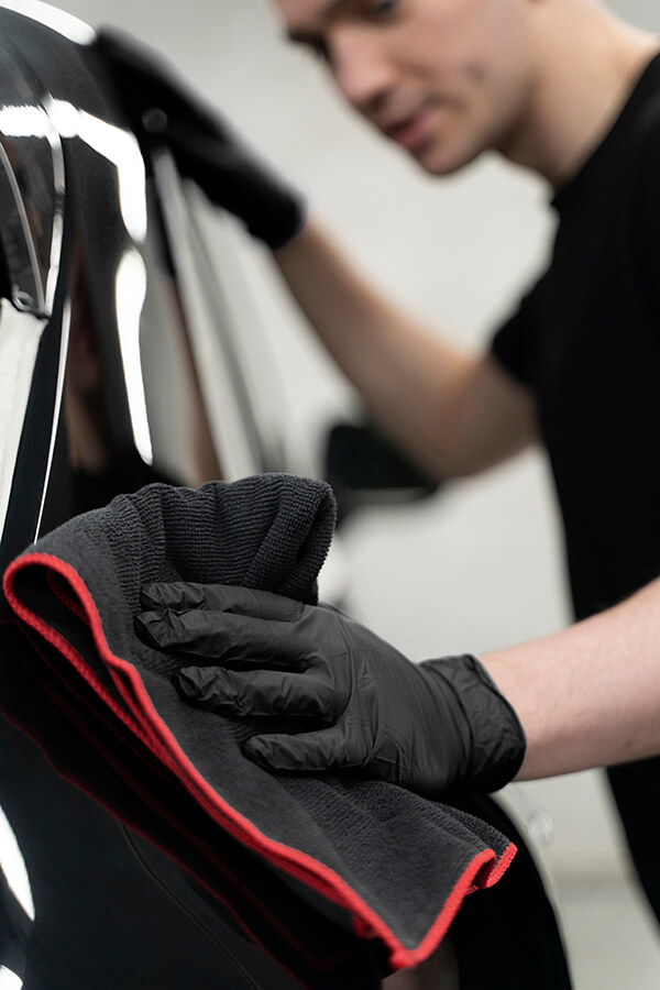 Gloved technician wiping a black vehicle with a microfiber cloth