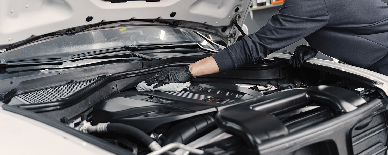 Gloved technician wiping an engine cover under an open hood