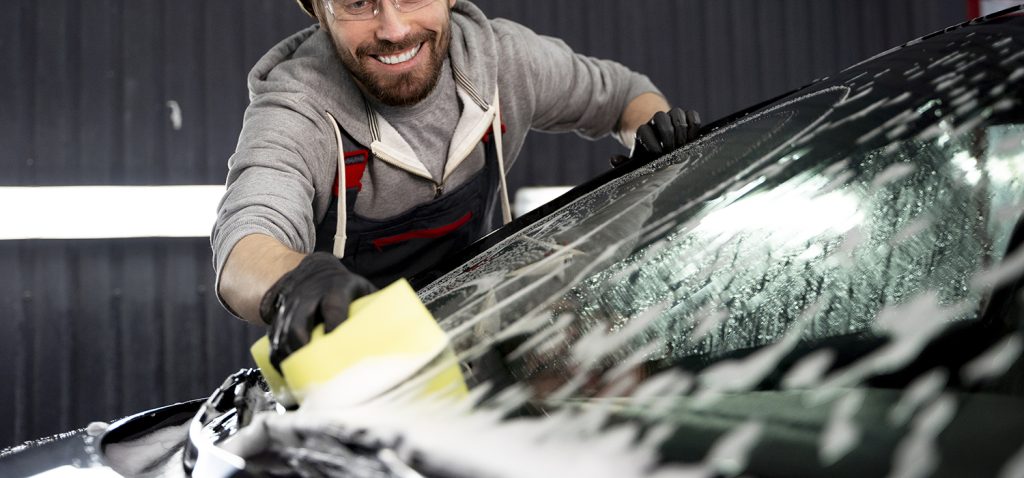 Technician washing a car windshield with a sponge