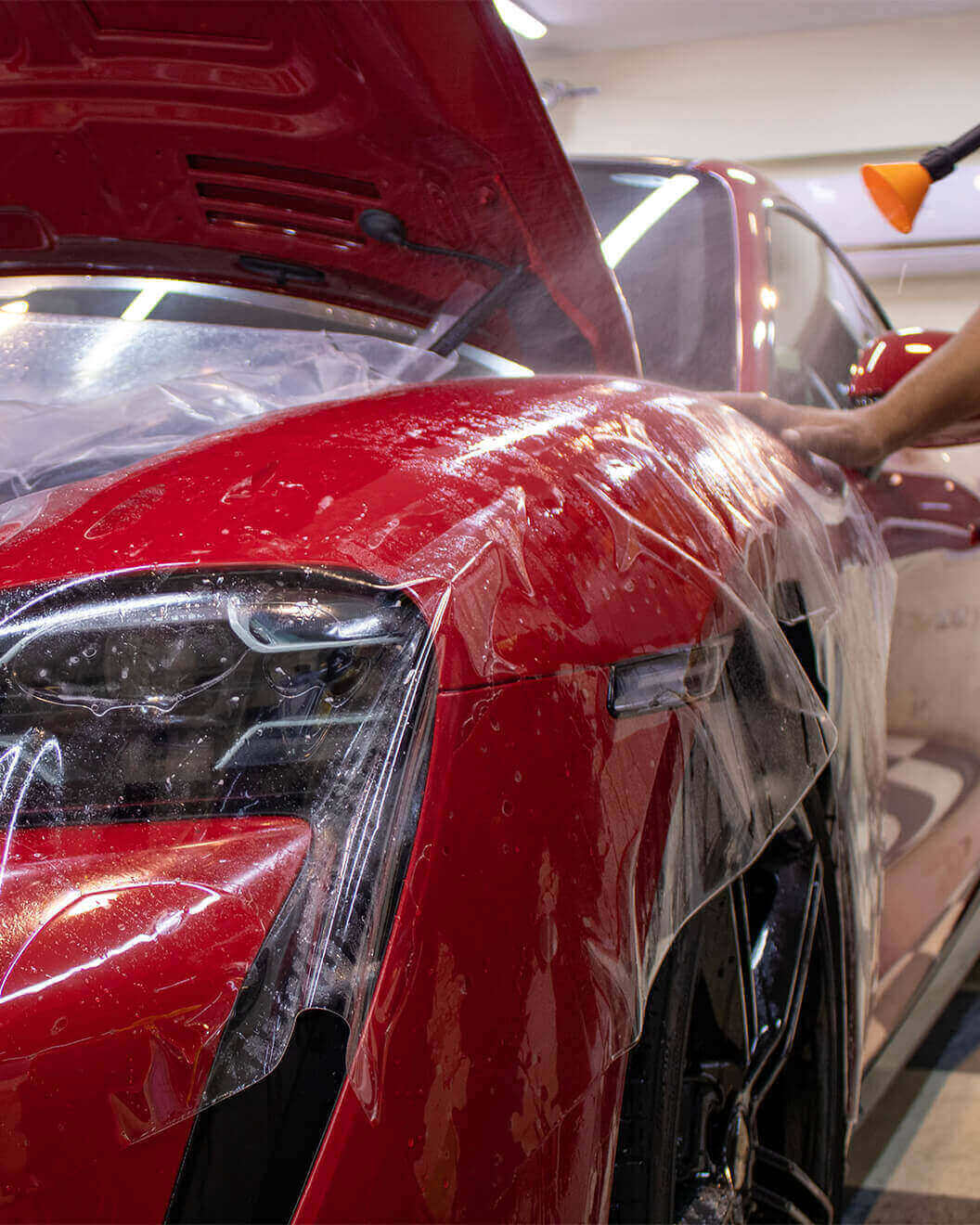 Clear protection film being fitted around the headlight and front fender of a red sports car