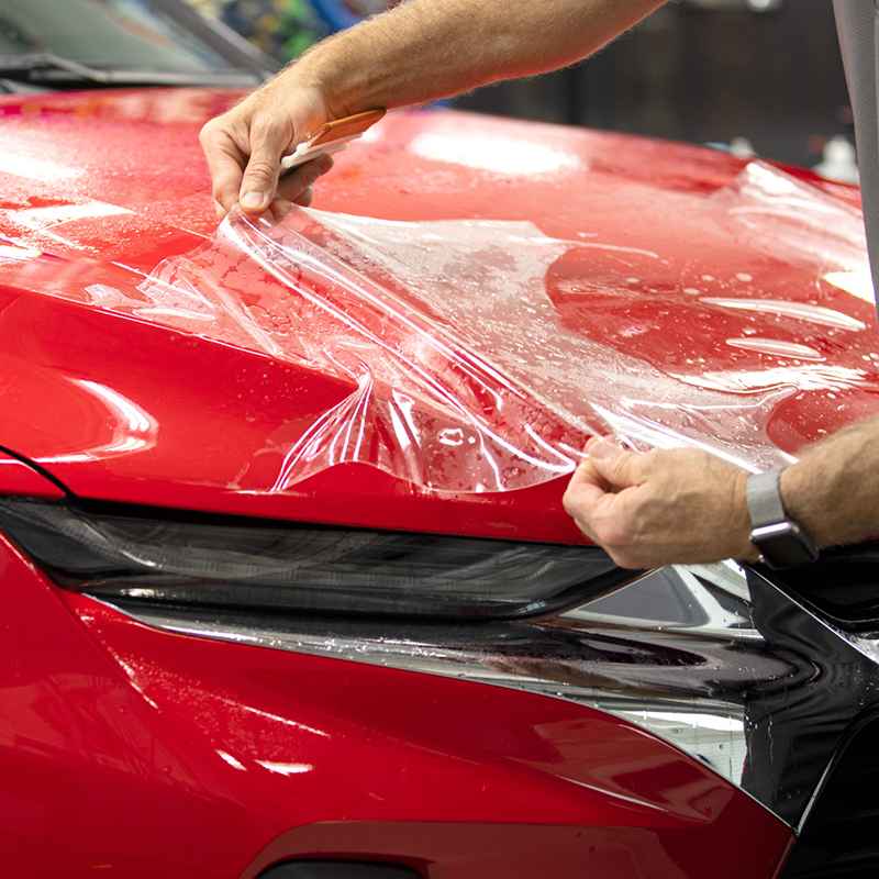 Clear protection film being positioned over a red car hood