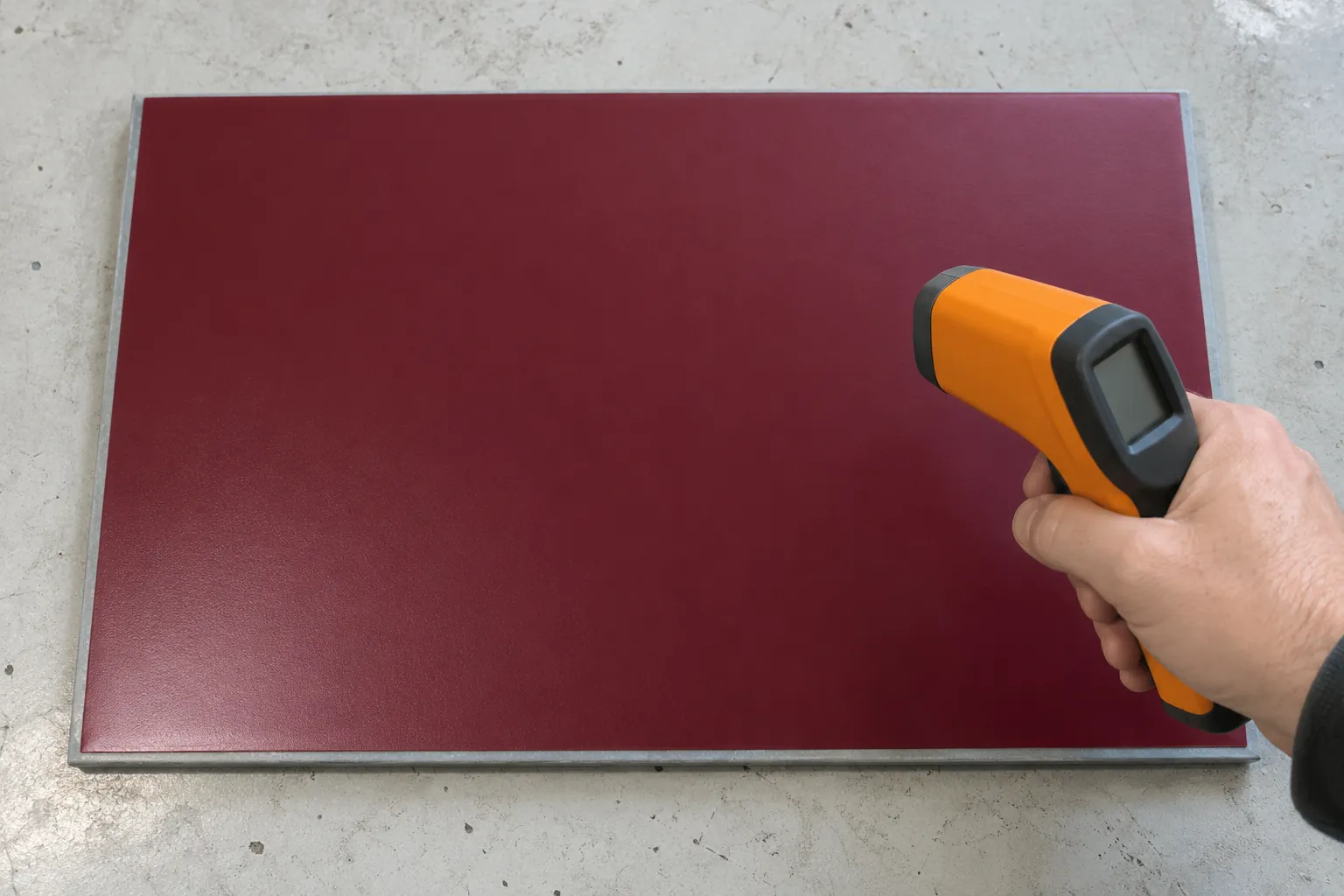 Infrared thermometer aimed at a burgundy vinyl practice panel on a workshop bench