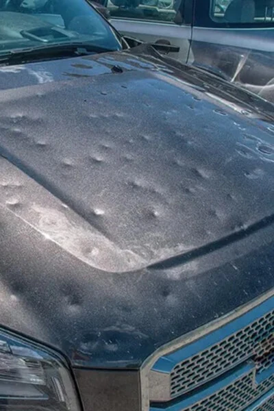 Multiple hail dents across a dark vehicle bonnet