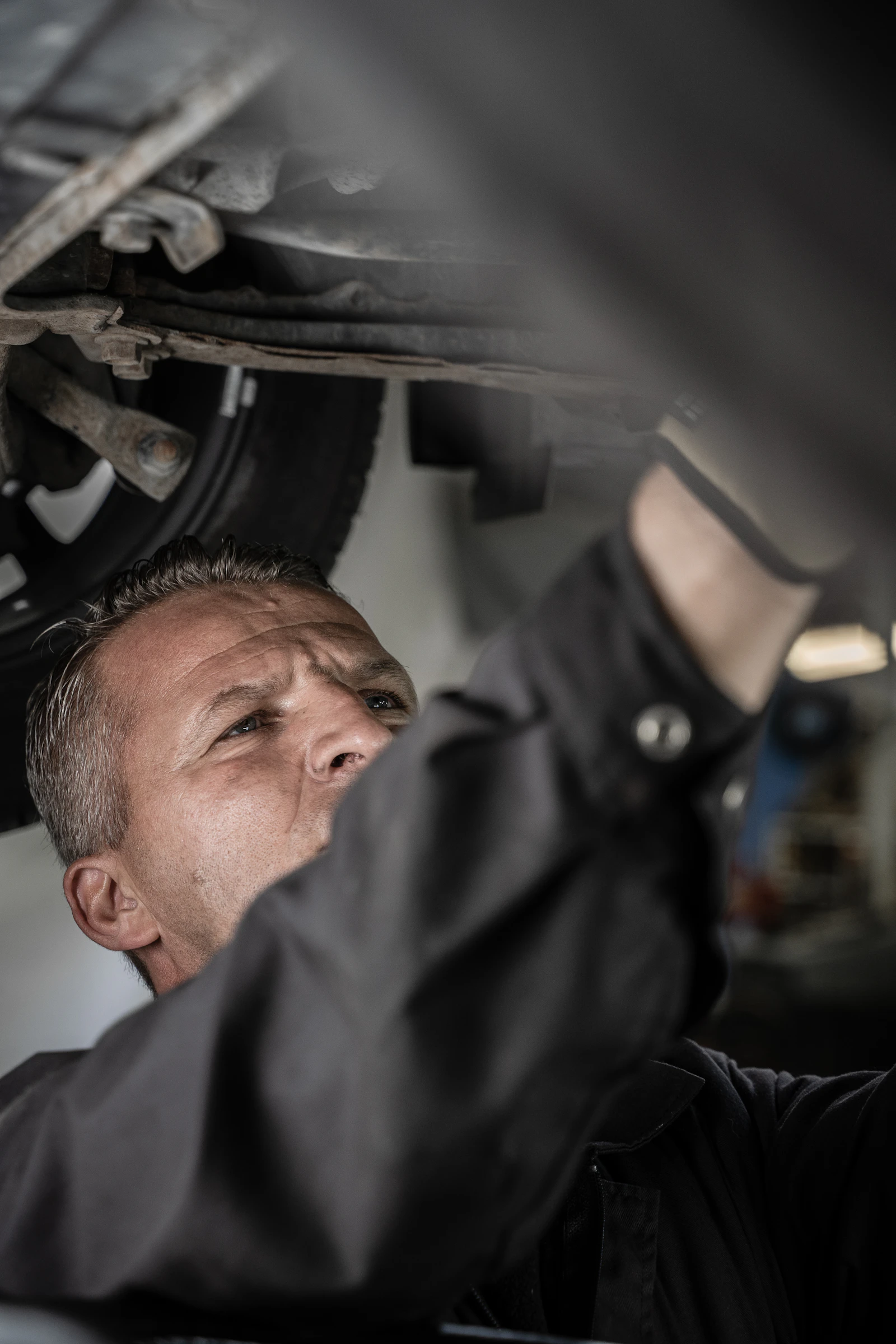 Mechanic assessing parts beneath a vehicle