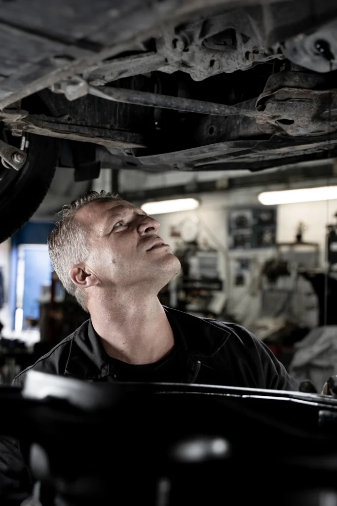Mechanic examining the accessible underside of a raised car