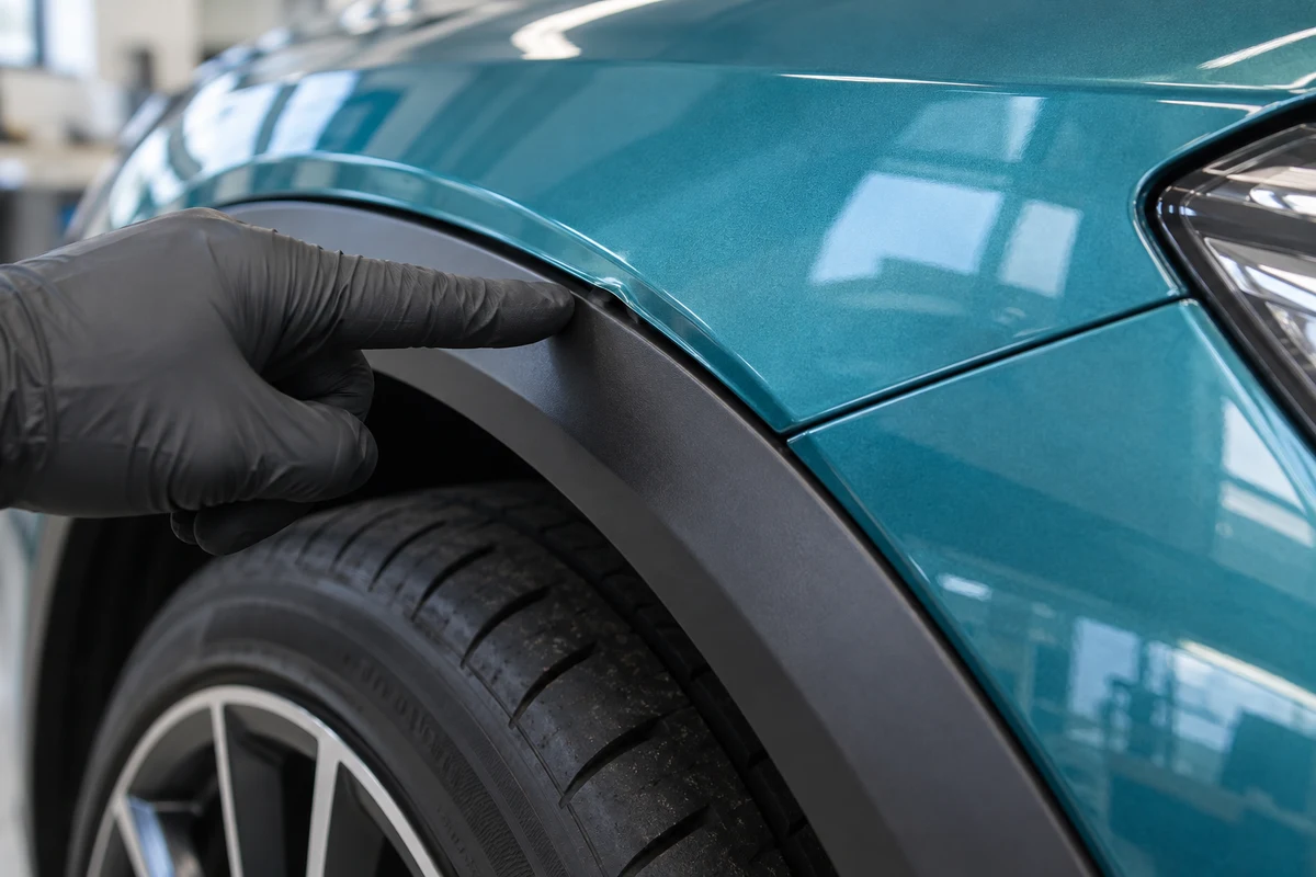 Gloved hand pointing beside a raised teal vinyl edge at a wheel arch